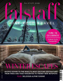 Falstaff International magazine cover featuring a winter escape with a person relaxing in bed beneath alpine windows and snowy trees plus wine food travel headlines